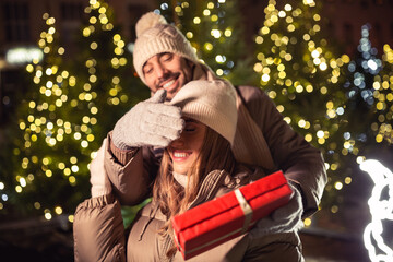 winter holidays and people concept - happy smiling couple with gift over christmas tree lights in evening city