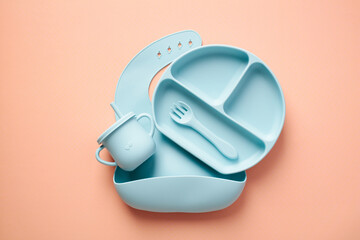Flat lay composition with silicone baby bib and dishware on peach color background. Serving baby...