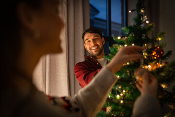winter holidays and people concept - happy couple decorating christmas tree at home