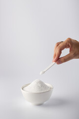 In his hand is a small spoonful of sugar substitute.
Vertical photo of a sugar substitute on a white background in a white bowl. Stevia.