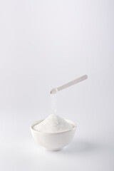 A small spoon pours the sugar substitute into the bowl. Vertical photo of a sugar substitute on a white background in a white bowl. Stevia.