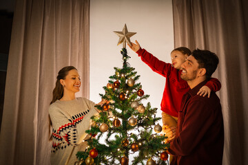 family, winter holidays and people concept - happy mother, father and little daughter decorating...