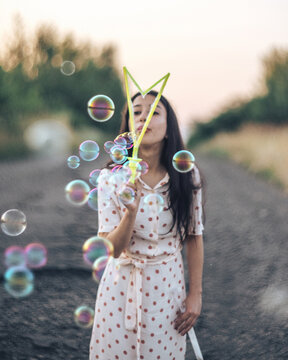 dark-haired girl blows soap bubbles