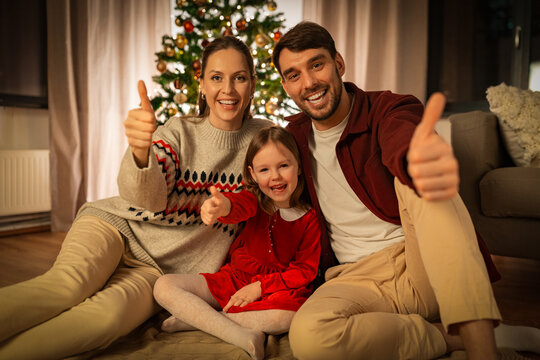 winter holidays, family and christmas concept - happy mother, father and little daughter showing thumbs up gesture at home