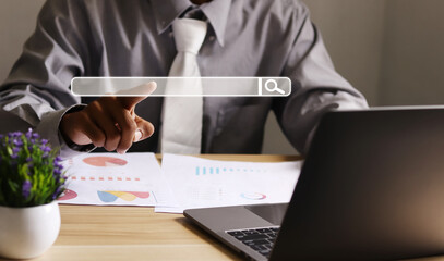 Businessman working on piles of paperwork and laptop pointing to an empty search bar search...