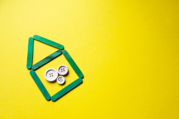 house from wooden green sticks on a yellow background, free space. Buttons of different sizes as a symbol of the family. Family in the house.