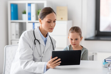 medicine, healthcare and pediatry concept - female doctor or pediatrician showing tablet computer to little girl patient at clinic