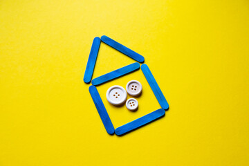 House made of blue sticks on a yellow background. Wooden buttons as a symbol of the family. Housing for Ukrainians. Ukraine flag colors