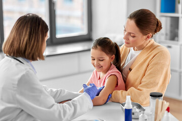 Fototapeta premium medicine, healthcare and pediatry concept - female doctor or pediatrician with syringe making vaccine injection to little girl patient at clinic