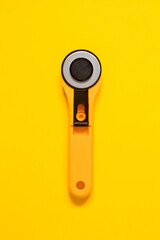 Yellow black rotary knife for patchwork on a yellow background. Sewing tool. Top view. Copy space.