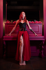 Beautiful girl in a corset posing with her foot on the piano with roses. Witch image. Halloween concept, nightclub, masquerade. Spain