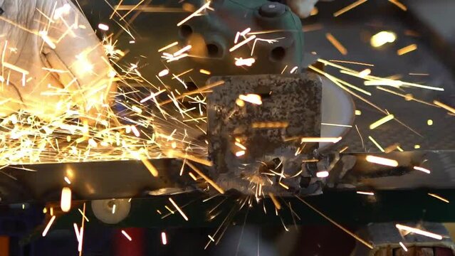 Slowmotion of a man welder with safety clothes polishes the metal angle grinder in the workshop, sideways flashes. Male hands in gloves cut a piece of iron with sparks fly in different directions.