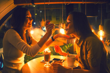 Two young women talking in the coffee shop during night out, eating chocolate dessert and drinking tea
