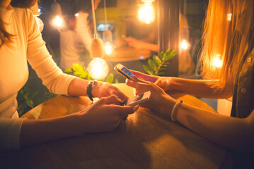 Two young women in the coffee shop using phones during night out