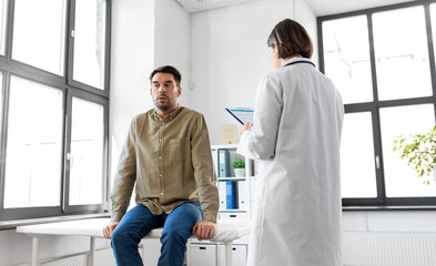 medicine, healthcare and people concept - female doctor with clipboard and male patient having health problem at hospital