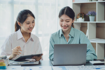 Obraz premium Smiling young Asian businesswomen talking to colleague and exchanging ideas together at office.