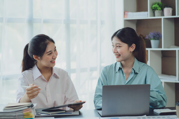 Obraz premium Smiling young Asian businesswomen talking to colleague and exchanging ideas together at office.