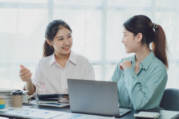 Obraz premium Smiling young Asian businesswomen talking to colleague and exchanging ideas together at office.