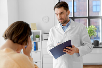 Obraz premium medicine, healthcare and people concept - male doctor with clipboard and fe male patient having health problem at hospital