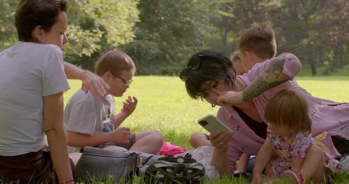 Large family at a picnic in the park. Mom communication with daughter. Use of gestures, family meeting. Using the phone in hand. CZ, Prague, Stromovka, 14.7.22.