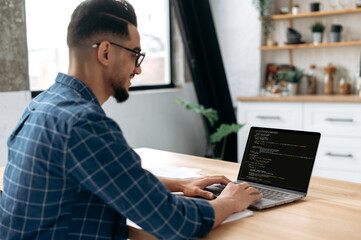 Side view of a programmer with laptop. Clever successful guy, an IT specialist, software developer, uses laptop, male programmer prescribes codes for an application, develops software. IT technology