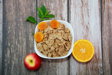 dry diet muesli in a white plate, orange slice, red apple and dried apricots