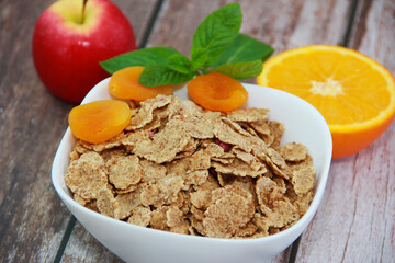 dry diet muesli in a white plate, orange slice, red apple and dried apricots