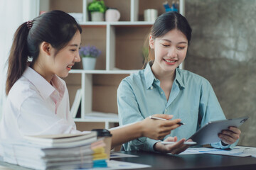 Obraz premium Smiling young Asian businesswomen talking to colleague and exchanging ideas together at office.