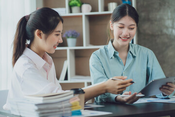 Obraz premium Smiling young Asian businesswomen talking to colleague and exchanging ideas together at office.