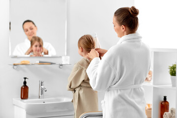 Obraz premium beauty, family and people concept - happy smiling mother and daughter looking to mirror and braiding hair in bathroom