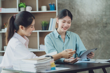 Smiling young Asian businesswomen talking to colleague and exchanging ideas together at office.