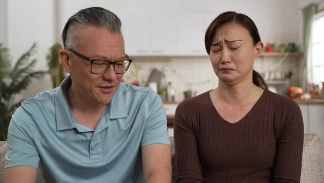 caring asian retired father consoling frustrated daughter and patting on her back in living room at home. the depressed woman cries and buries her face in hands while listening