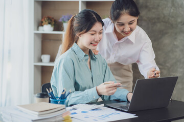 Obraz premium Two young Asian businesswoman discuss investment project working and planning strategy. Business people talking together with laptop computer at office.