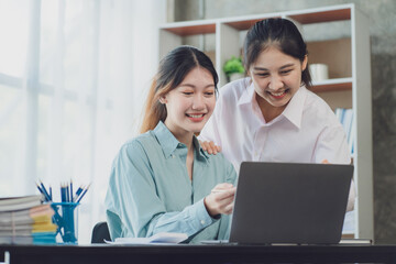 Two young Asian businesswoman discuss investment project working and planning strategy. Business people talking together with laptop computer at office.