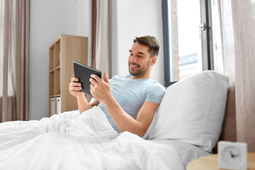 technology, internet and people concept - man with tablet pc computer in bed at home bedroom