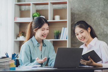 Two young Asian businesswoman discuss investment project working and planning strategy. Business people talking together with laptop computer at office.