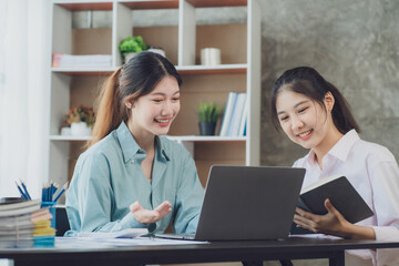 Obraz premium Two young Asian businesswoman discuss investment project working and planning strategy. Business people talking together with laptop computer at office.