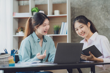 Obraz premium Two young Asian businesswoman discuss investment project working and planning strategy. Business people talking together with laptop computer at office.