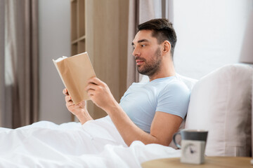 people and rest concept - man reading book in bed at home