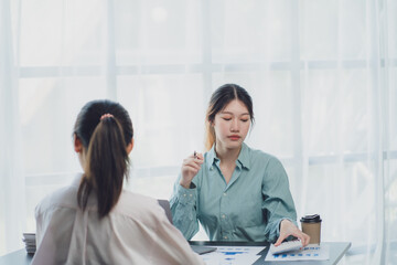 Two young Asian businesswoman discuss investment project working and planning strategy. Business people talking together with laptop computer at office.