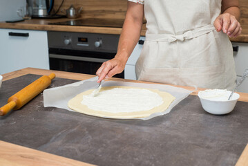 A woman hands are smearing creamcheese on dough. Preparation of pizza.