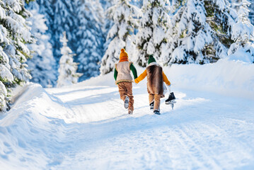 Winter family walk along a wonderful snowy forest road. Children run snow, back view. Sunny winter day. - obrazy, fototapety, plakaty