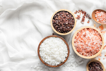 A clear cup of different types of cooking salt is placed on a white cloth.