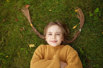 Happy smiling young girl with funny pigtails lying on green grass background