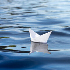 white paper boat floats on the water, go on a trip,  origami small boat on blue water,  square frame