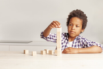 Portrait of cheerful child small boy playing and building a tower of wooden blocks in white interior