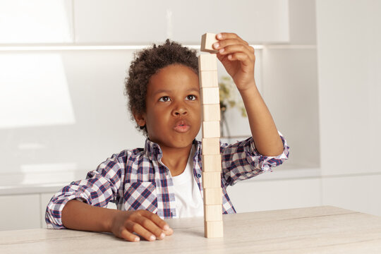 Cute clever child small boy playing and building a tower of wooden blocks at home