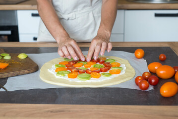 A woman hands laying out tomatoes on dough. Preparation of pizza or pie.