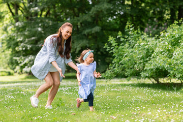 Fototapeta premium family, motherhood and people concept - happy mother with little daughter playing at summer park or garden