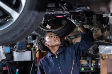 African American mechanic woman changing car engine, working underneath vehicle at auto repair shop